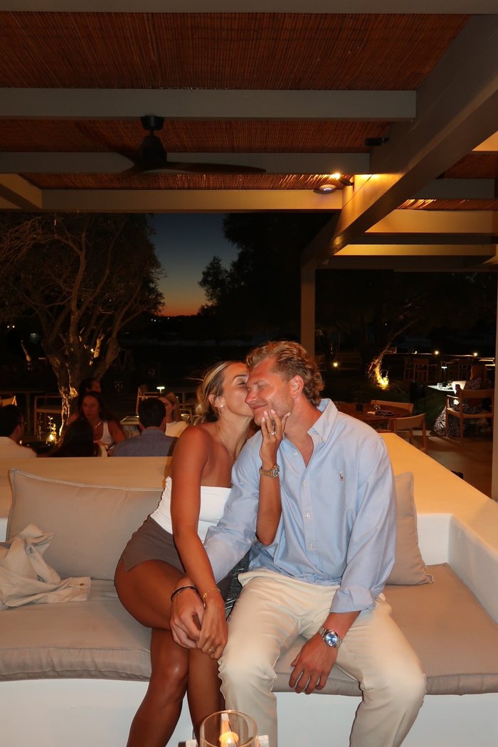 Taylor kissing Jared on the cheek on an outdoor restaurant sofa at night.