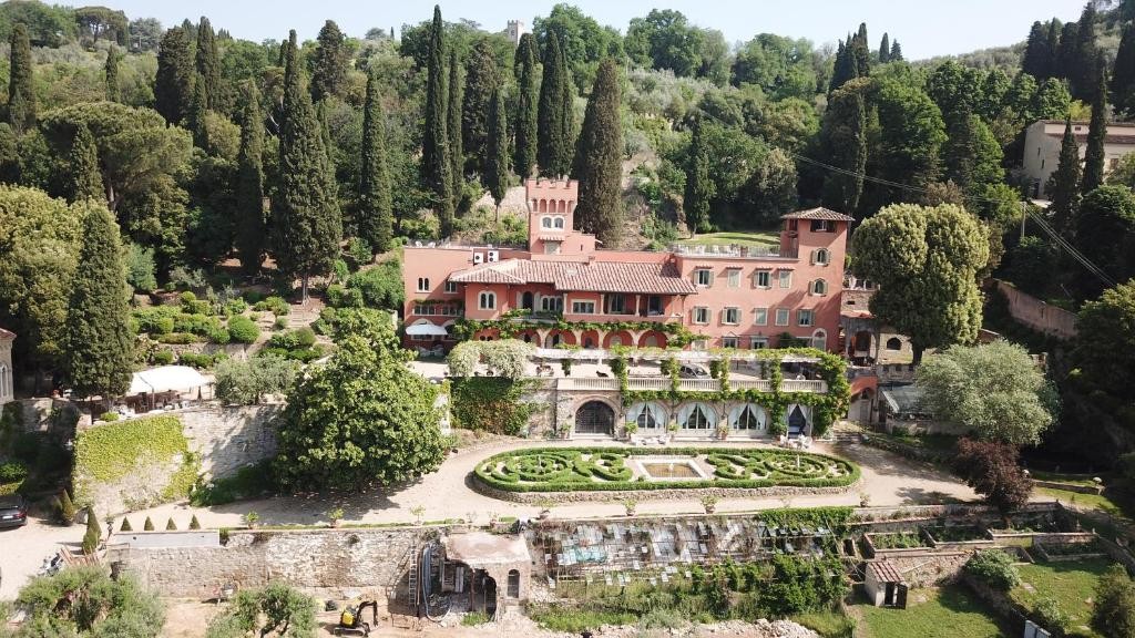 Aerial view of Villa Le Fontanelle, a rose-colored Tuscan villa surrounded by cypress trees with formal gardens below.